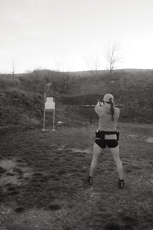 Black and white photograph of a competitor facing steel and paper targets at a Texas shooting range